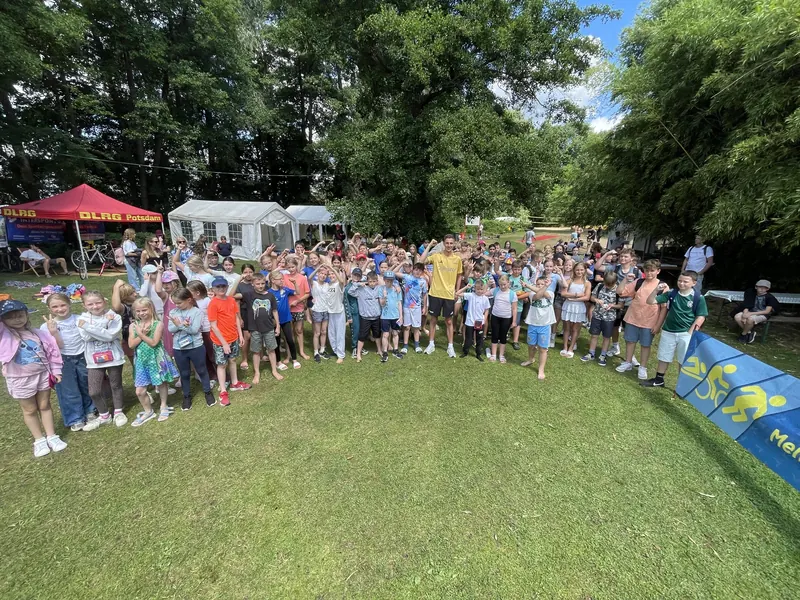 Große Gruppe winkender Kinder auf der Wiese, dahinter das DLRG-Zelt